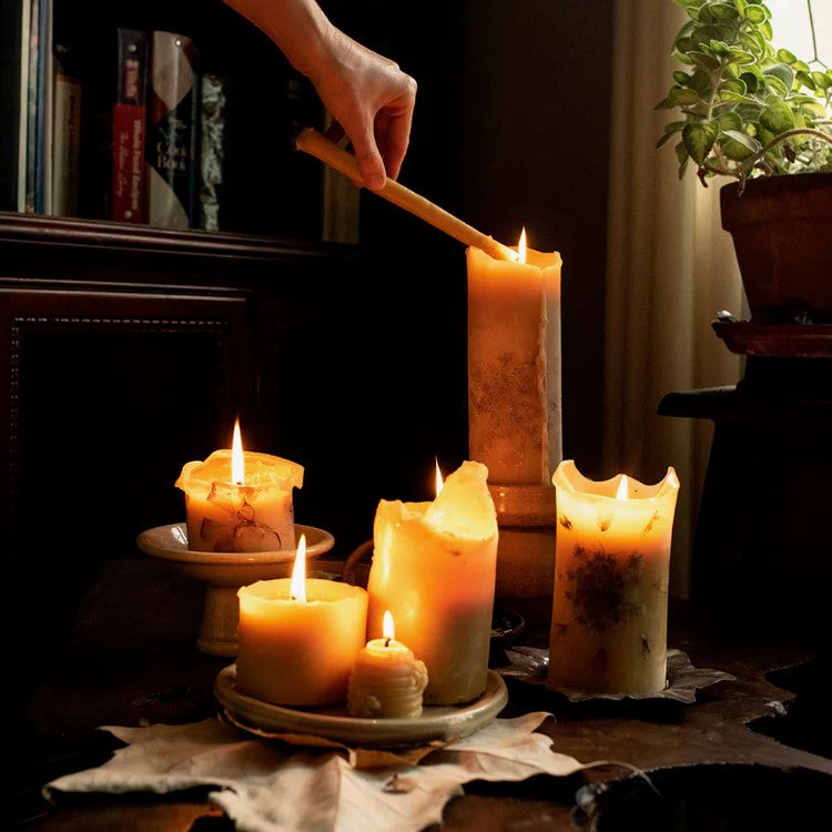 Woman's hand lights a grouping of six pillar candles of various sizes illuminating a cozy room