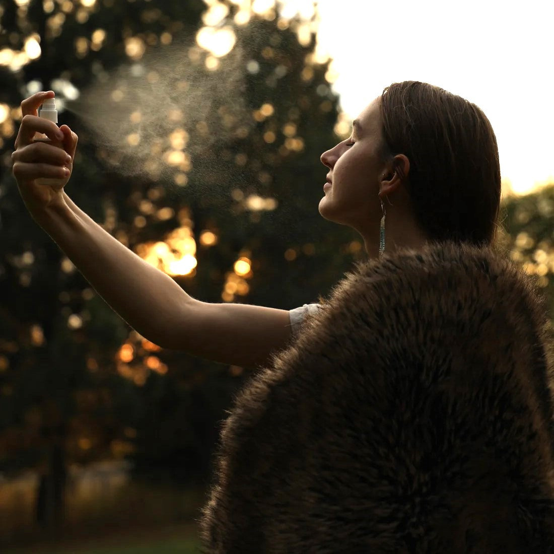 Young woman standing outdoors mists herself with a moisturizing hydrosol from Forage Folk