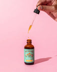 Bottle of Poppy Dream Elixir with hand holding dropper above.