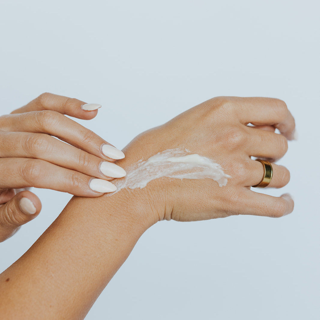 Person applying cream to their wrist against a light background