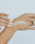 Person applying cream to their wrist against a light background