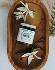 Jar of 'Whipped Tails' with vanilla beans and flowers on a wooden tray