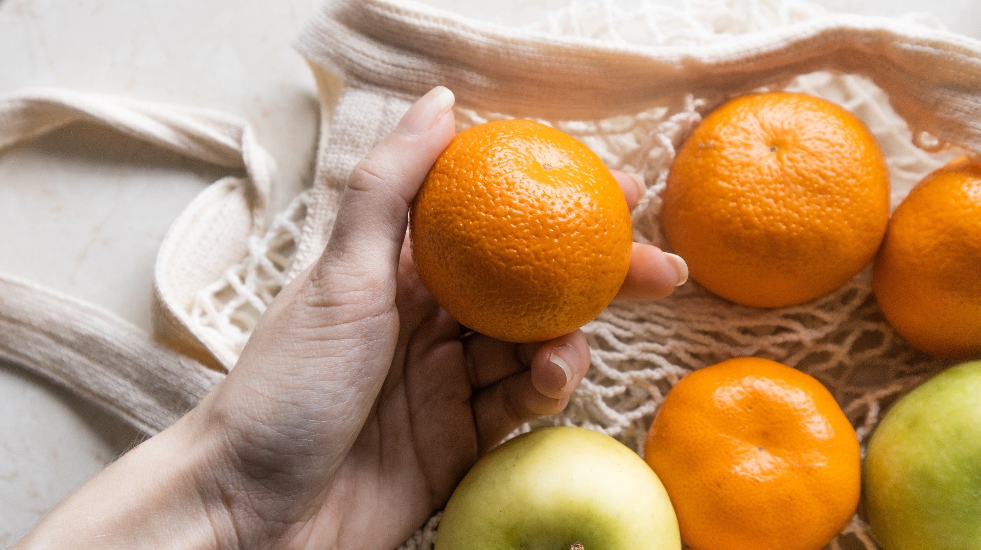 A woman holds an orange and plastic-free produce bag. Plastic-free home.