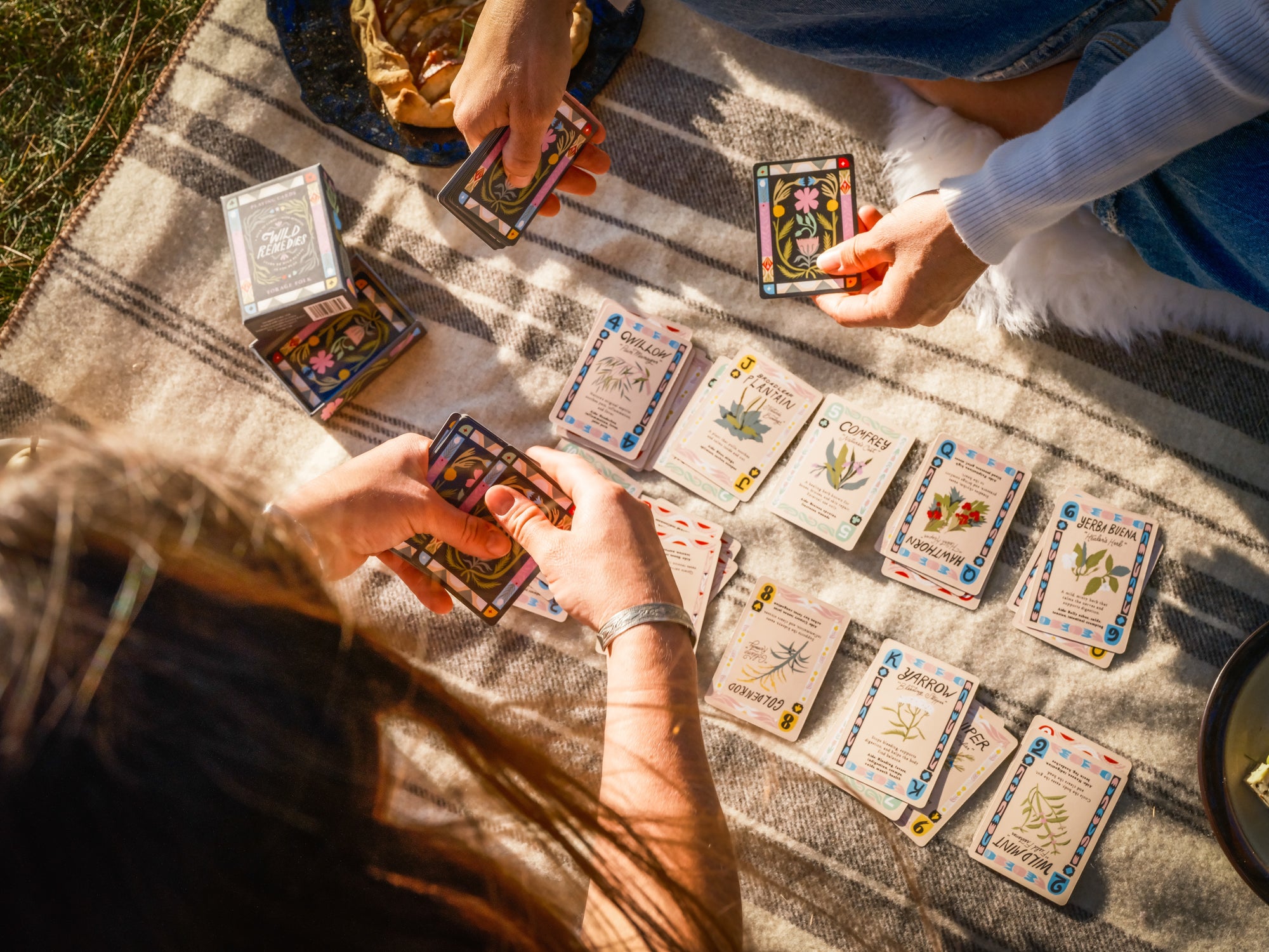 Two people playing a nature card game on a blanket outdoors