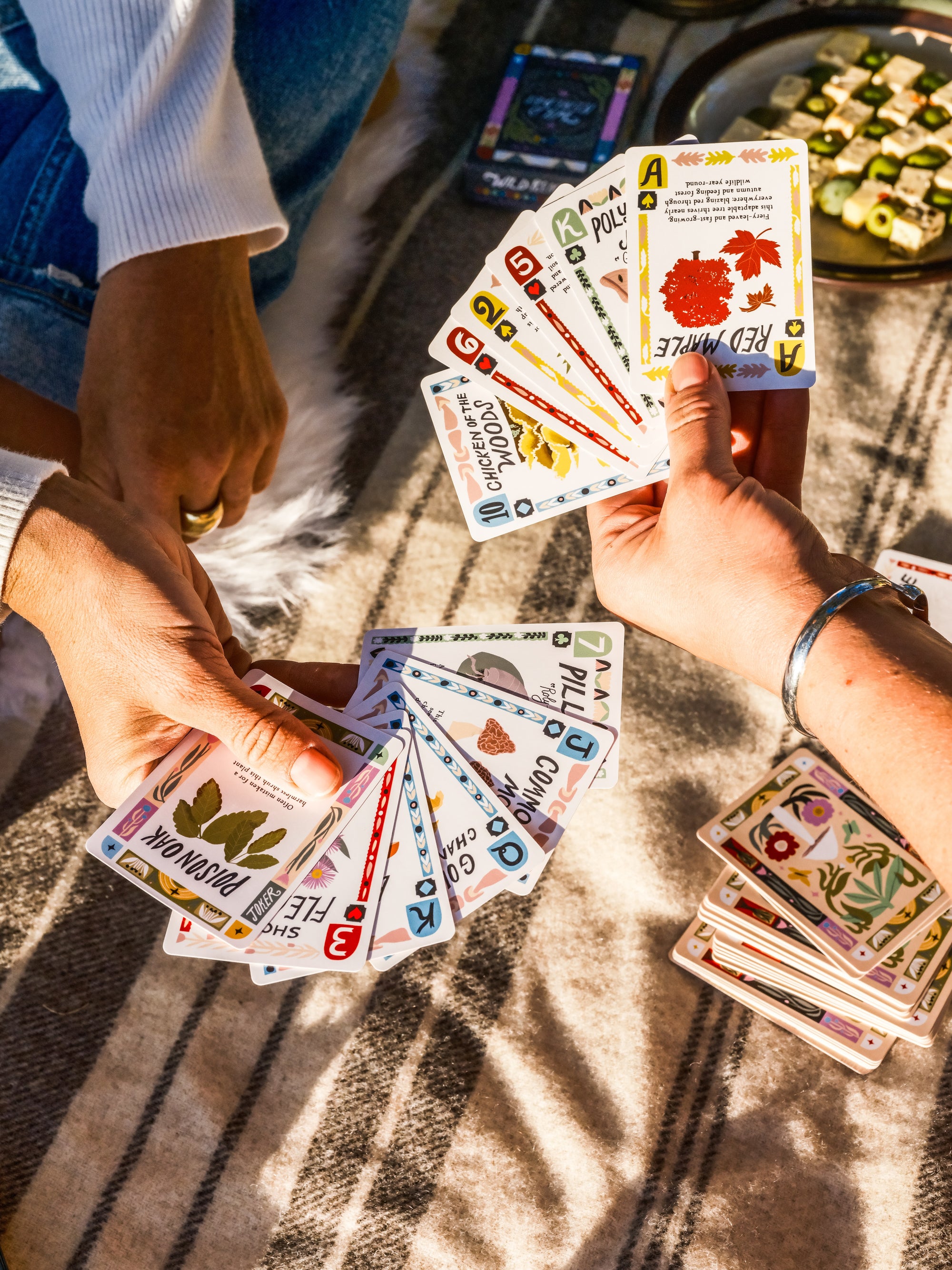 Two people playing a nature card game on a blanket outdoors