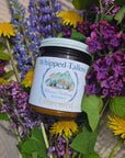 Jar of whipped tallow nestled among purple and yellow flowers on a textured surface